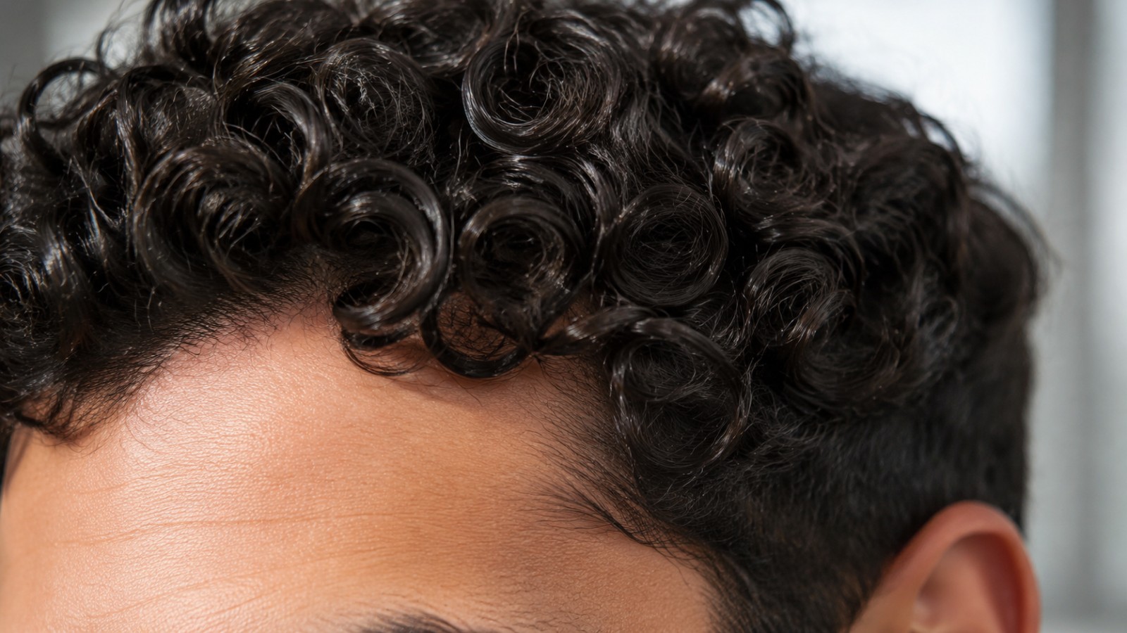 A close look at defined curl clumps, where the raised cuticle at every bend explains why textured hair dries out so quickly.